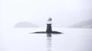 white and black lighthouse on black rock surrounded by water