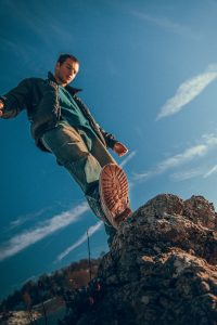 Man stepping on a rock under blue sky