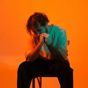a man sitting on top of a chair in front of an orange wall
