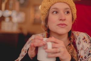 woman in brown knit cap holding white ceramic mug