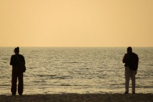 Two people standing on a beach watching the ocean