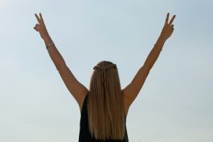 Woman celebrates with a peace sign against the sky.